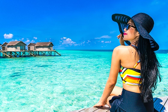 Woman Relaxing on Tropical Deck Overlooking Turquoise Water and Bungalows